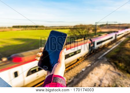Day View Of Woman Hand Holding Smartphone Over Uk Railroad.
