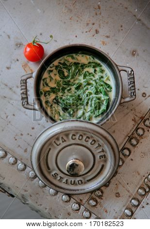 Creamy soup with spinac in a tureen and a cherry tomato