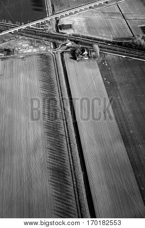 Black and white aerial view of green fields with a farm house a canal and motorway road in The Netherlands.