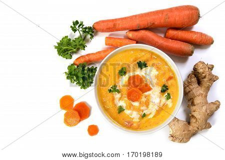 Carrot cream soup with ingedients ginger root raw carots and parsley garnish areal view from above isolated on a white background with copy space