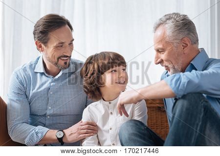 Pleasant interaction. Handsome delighted pleasant grandfather looking at his grandson and speaking with him while spending time with his family members