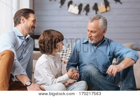 Family greetings. Cheerful positive elderly man shaking his grandsons hand and smiling while greeting him