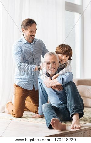 Care and love. Happy cute young boy standing behind his grandfather and hugging him while expressing his love for him