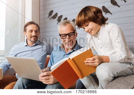 Reading a story. Happy young cute boy holding a book and showing it to his grandfather while reading a story