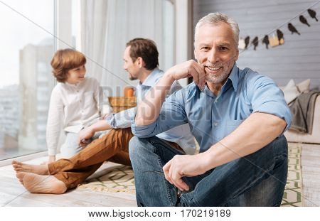 Positive emotions. Cheerful delighted nice man holding his chin and smiling while being together with his family
