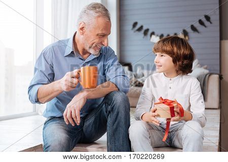 Thank you for the present. Pleasant nice delighted child holding a present box and looking at his grandfather while being grateful for the present
