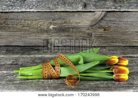 Tied with a measuring tape bouquet of tulips flowers on a wooden background. Spring flowers. Women's Day background with flowers. Concept is spring time to slim.