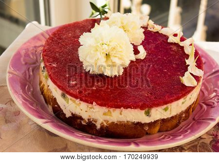 Closeup of a strawberry cake from side on white batskground sponge cake with jelly and fruit on the background of the railing. decorated with white flowers