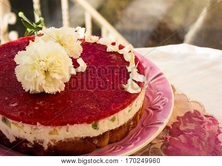 Closeup of a strawberry cake from side on white batskground sponge cake with jelly and fruit on the background of the railing. decorated with white flowers