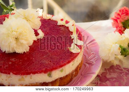Closeup of a strawberry cake from side on white batskground sponge cake with jelly and fruit on the background of the railing. decorated with white flowers