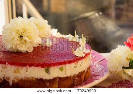 Closeup of a strawberry cake from side on white batskground sponge cake with jelly and fruit on the background of the railing. decorated with white flowers