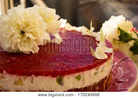 Closeup of a strawberry cake from side on white batskground sponge cake with jelly and fruit on the background of the railing. decorated with white flowers