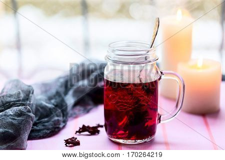 Hibiscus tea in glass Cup. The candles in the background. Tea strainer nearby. Light background. Selective focus