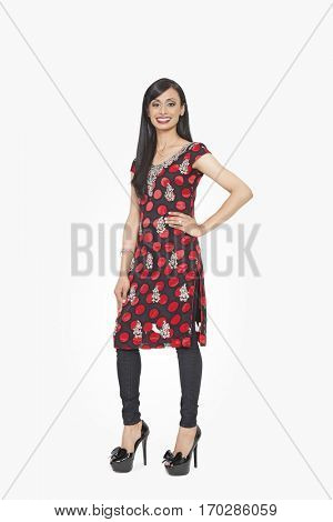Full length portrait of Indian female in traditional wear standing with hand on hip over gray background