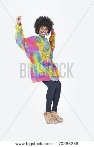 Full length portrait of happy African American woman in dashiki dancing over gray background
