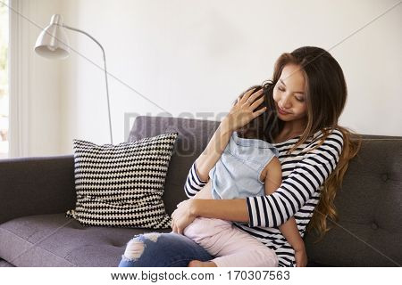 Mother Cuddling Daughter On Sofa At Home