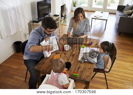 Mother Uses Laptop Whilst Father Plays With Children At Home