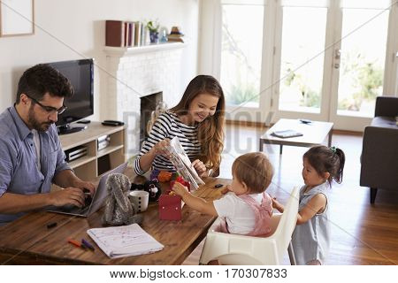 Father Uses Laptop Whilst Mother Plays With Children At Home