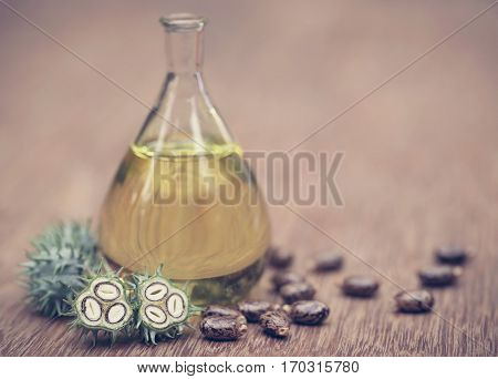 Castor oil with dry and green beans on wooden surface