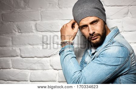 Trendy man in woolly hat standing against white brick wall. Looking at camera, copyspace.