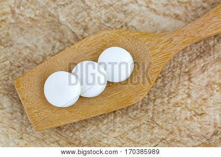 Top view of 3 white medicines on wooden spoon with brown Mulberry paper background