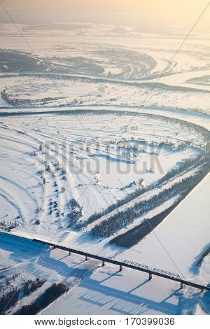 Aerial view of snow covered winter landscape of river valley and train, which crossing river on bridge