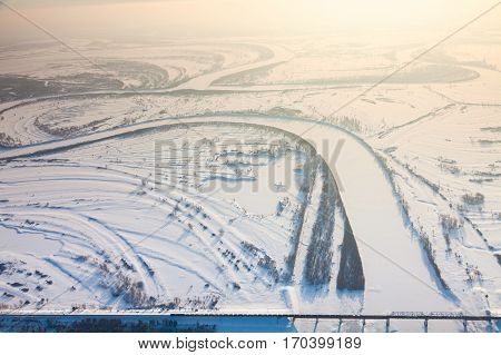 Aerial view of snow covered winter landscape of river valley and train, which crossing river on bridge