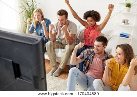 friendship, leisure, people and entertainment concept - happy friends with remote control and drinks watching tv at home