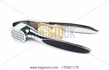 Metal garlic press utensil next to a pile of fresh cloves isolated over the white background