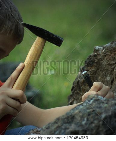 A little mineral collector with hammer and chisel at work