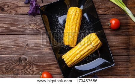 Corn on the black plate on wooden table. Helthy food.