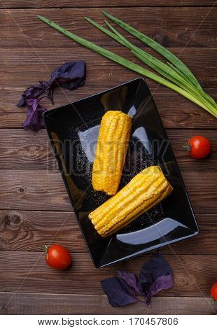 Corn on the black plate on wooden table. Helthy food.