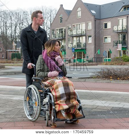 Man pushing a woman in a wheelchair at a zebra crosssing in a Dutch village