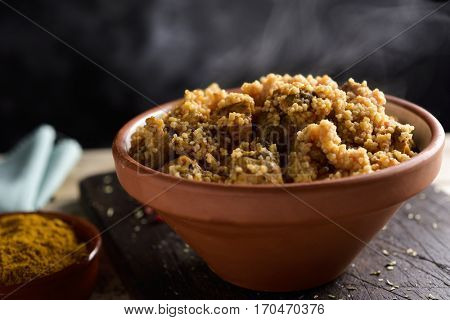 closeup of an earthenware casserole with couscous with chicken and vegetables on a rustic wooden table