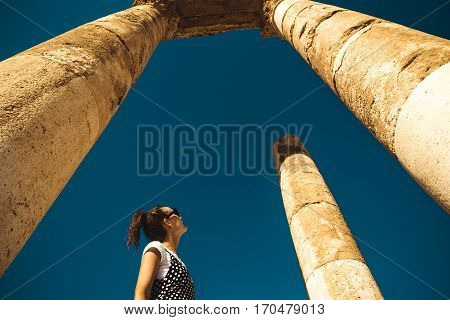 Photo of the Female tourist stand between columns exploring Hercules Temple remains on Amman Citadel hill. Ancient ruins. Travel concept. Tourist attraction. Woman looks up dreaming about adventure. Copy space.