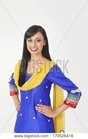 Portrait of beautiful Indian woman in traditional wear standing with hands on hips over gray background