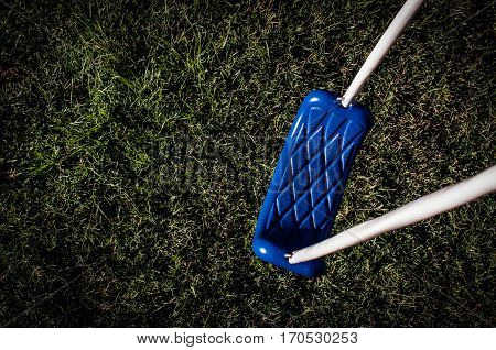 Blue swing in hard light with green grass below