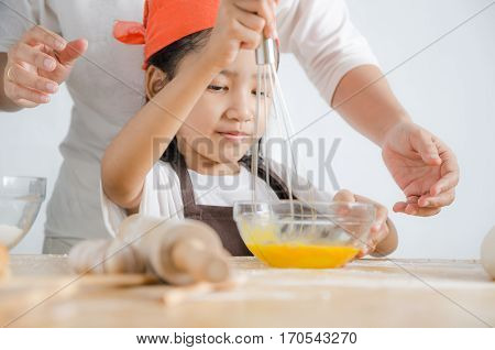 Asian little girl using stainless steel whisk to mix the egg for making bakery with mom