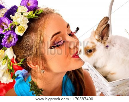 Easter girl holding bunny and eggs. Woman with holiday spring flowers hairstyle and make up kissing rabbit . White background. Makeup with fake eyelashes.