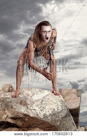 Wild man stands on a rock on grey sky background