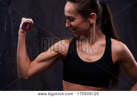 Close-up of determined woman during persevering training in the dark studio. Long-haired brunette practicing exercise with dumbbells indoors. Abdominal muscle breathing exercises