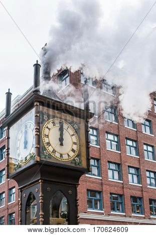 The historic steam clock strikes midday in Gastown downtown Vancouver with jets of steam rising from the clock