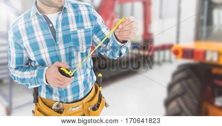 Mid section of handyman with tool belt and measuring tape in workshop
