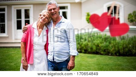 Hearts hanging on a line against senior couple with arms around standing in yard
