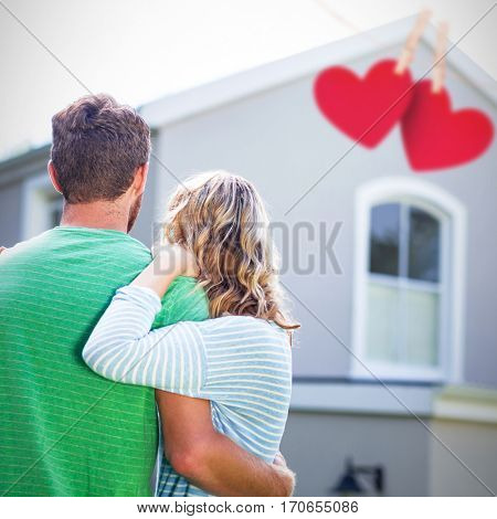 Hearts hanging on a line against couple standing against house