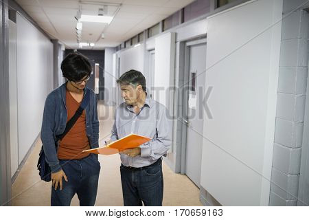 Professor with notebook talking to a student in corridor