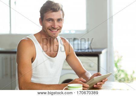 Portrait of smiling young man using tablet PC at breakfast table in kitchen