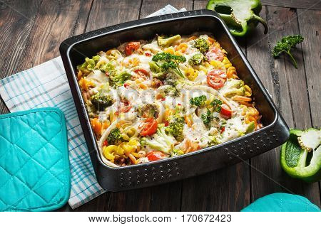 Baked pasta with broccoli and cheesy tomato sauce on wood background.