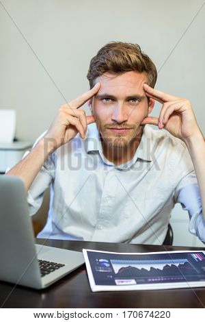 Portrait of frustrated businessman sitting by table in office