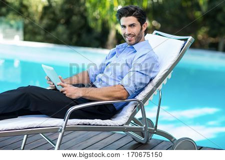 Portrait of smart man relaxing on sun lounger and using a digital tablet near the pool